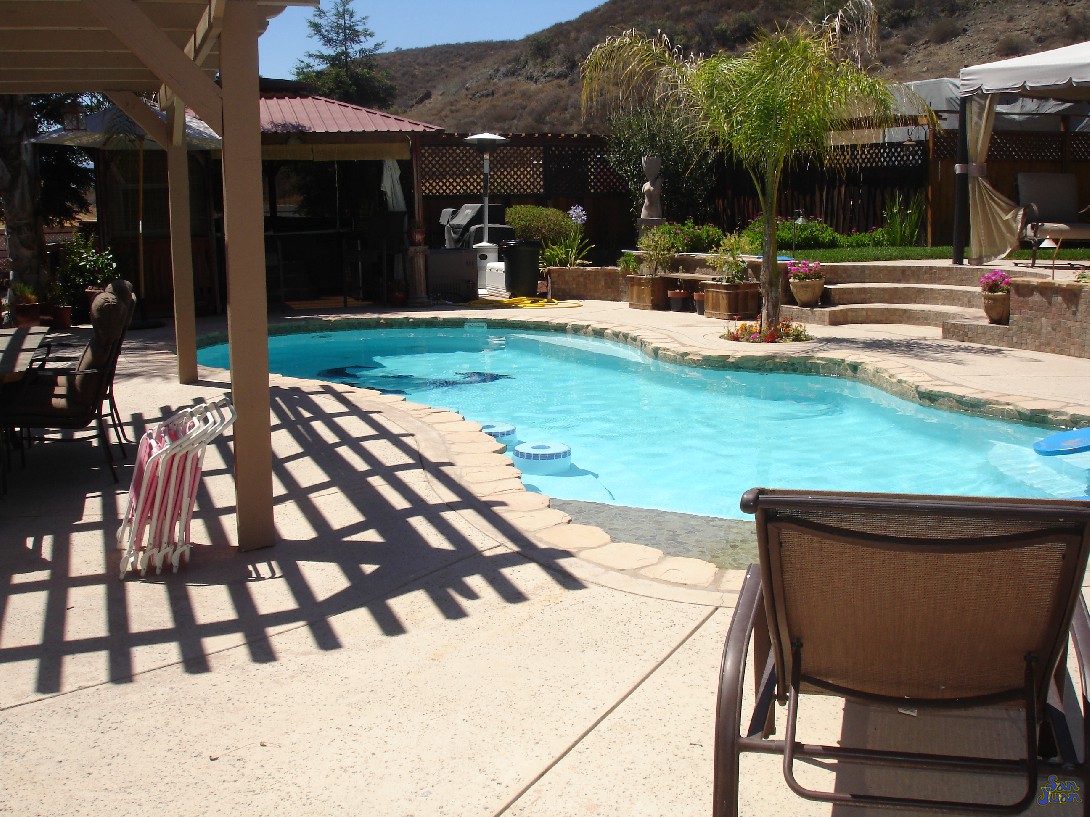 pleasure island fiberglass pool shape with attached spa and raised waterfalls next to outdoor kitchen