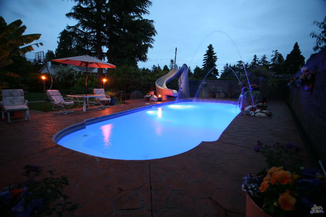 savannah deep pool shape at night with led lighting laminar jets slide and stamped stained concrete