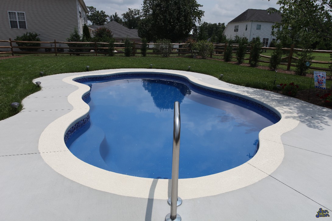 We love this gorgeous image of a Rio fiberglass shell with a Blue Lagoon gel coat. This image shows all of the modest curves from its free form design. This pool is built with a cantilever deck & stained concrete finish. As you can see here, adding a little more investment in a well poured deck goes a long way to boost the beauty of this swimming pool!