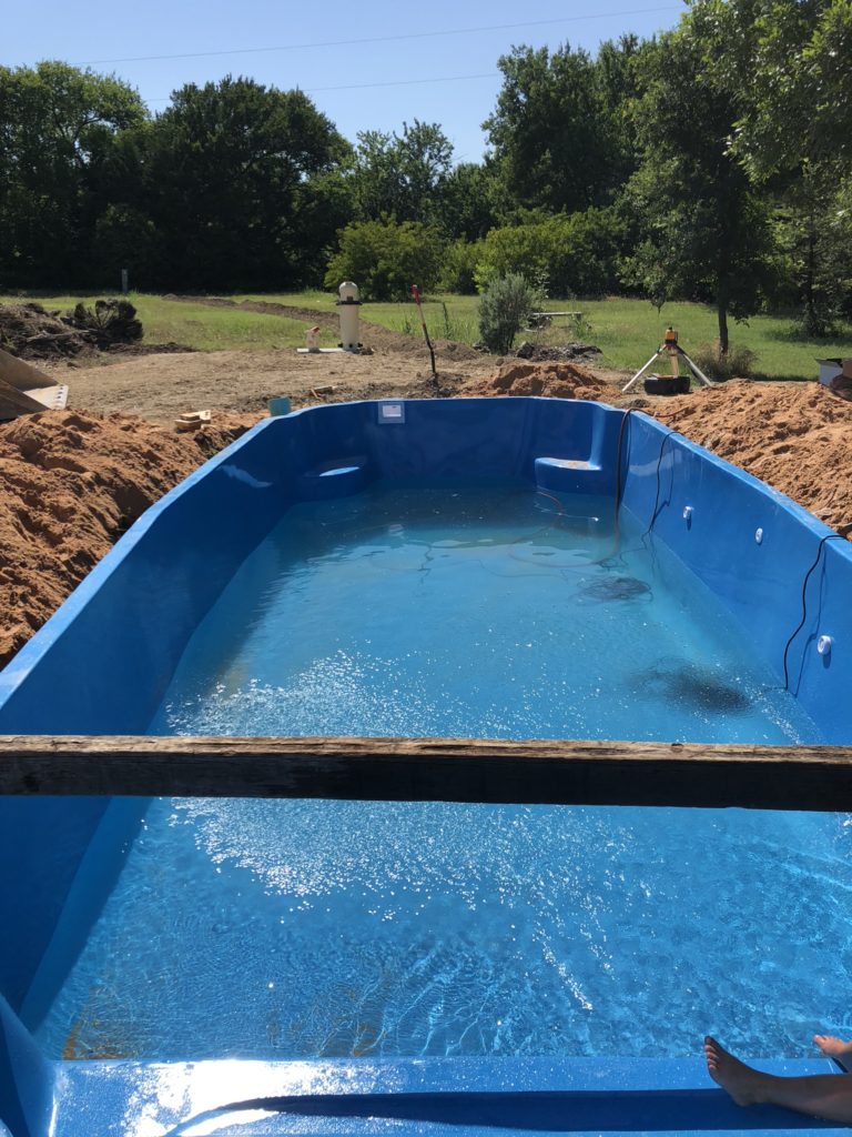 After we set our pool in our pre-dug hole, we slowly fill the pool shell with water. We must be careful during this stage to ensure that we do not knock the shell out of level. We take great care and re-shoot our elevations as the pool fills up and back fill to match the level of our water. 