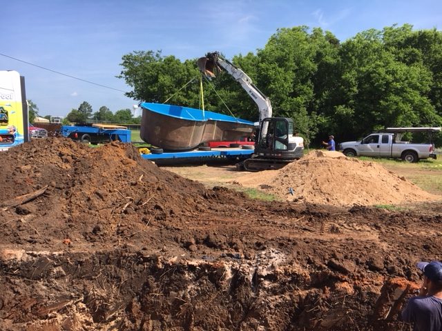 Did someone call for a Seaside fiberglass pool? We suppose this is the correct delivery address... especially since we see a lot of exposed dirt! Alright then, load er' up boys! You can see our excavator rig lifting this fiberglass shell right off this flatbed trailer. We are using the same machine that we excavated the hole to set your swimming pool. That's how things go with fiberglass; we are nifty and very resourceful!